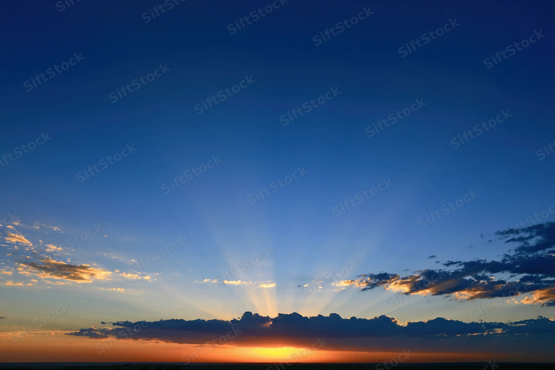 Crepuscular rays bursting upward from the horizon during sunset over a cloud-lined sky
