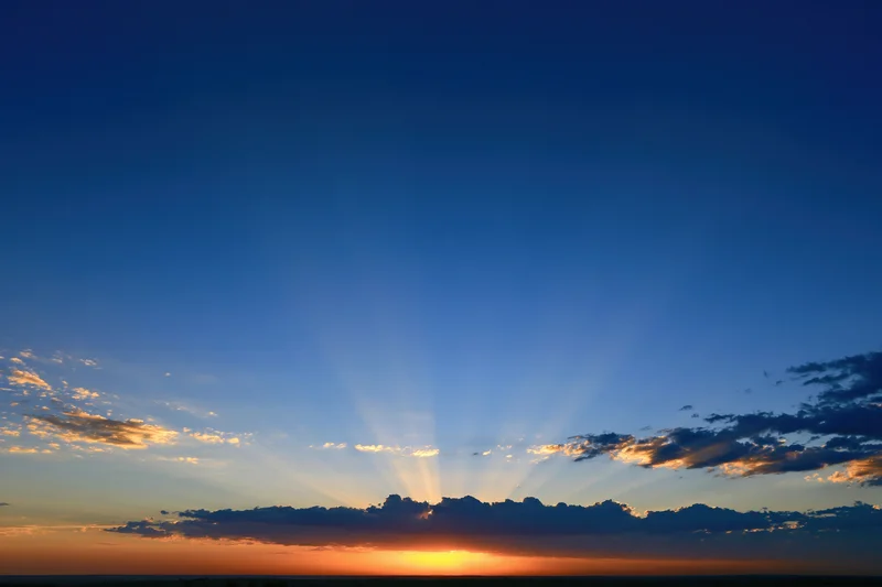 Crepuscular rays bursting upward from the horizon during sunset over a cloud-lined sky