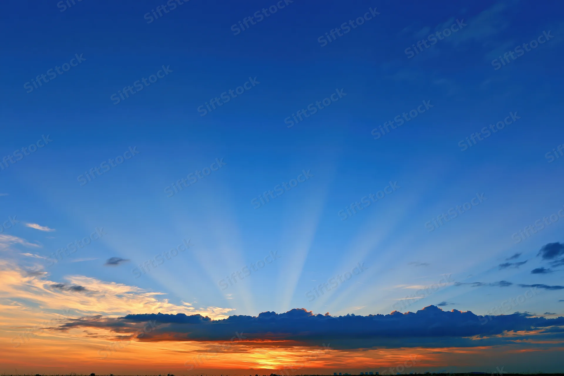 Crepuscular rays bursting upward from cloud layer at sunset horizon
