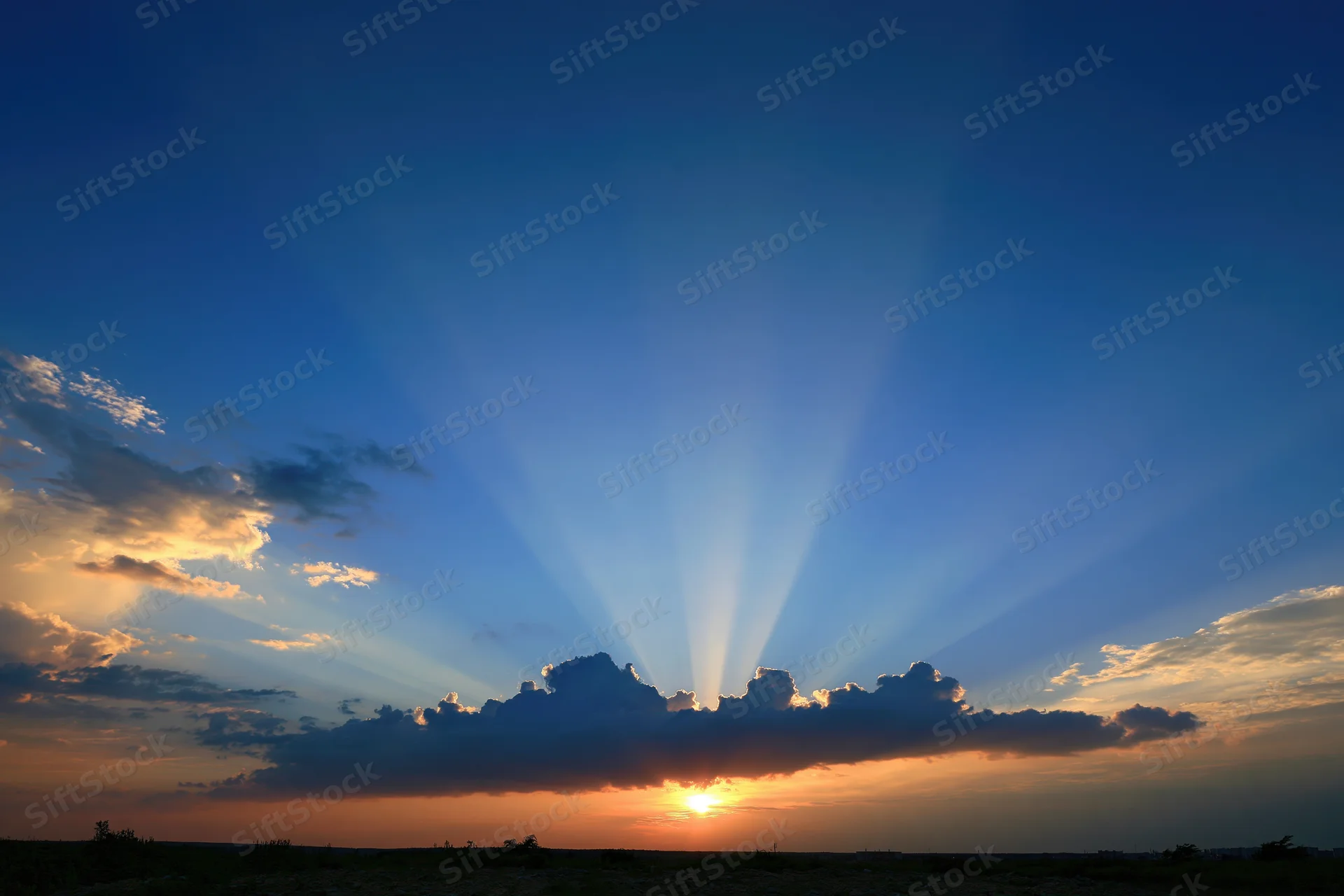 Crepuscular rays bursting upward from clouds at sunset over horizon