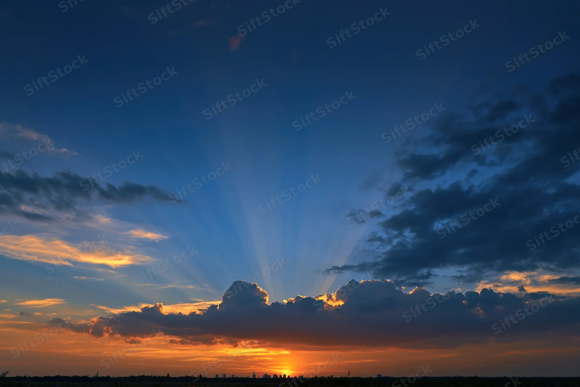 Crepuscular rays bursting upward from clouds at sunset over city skyline