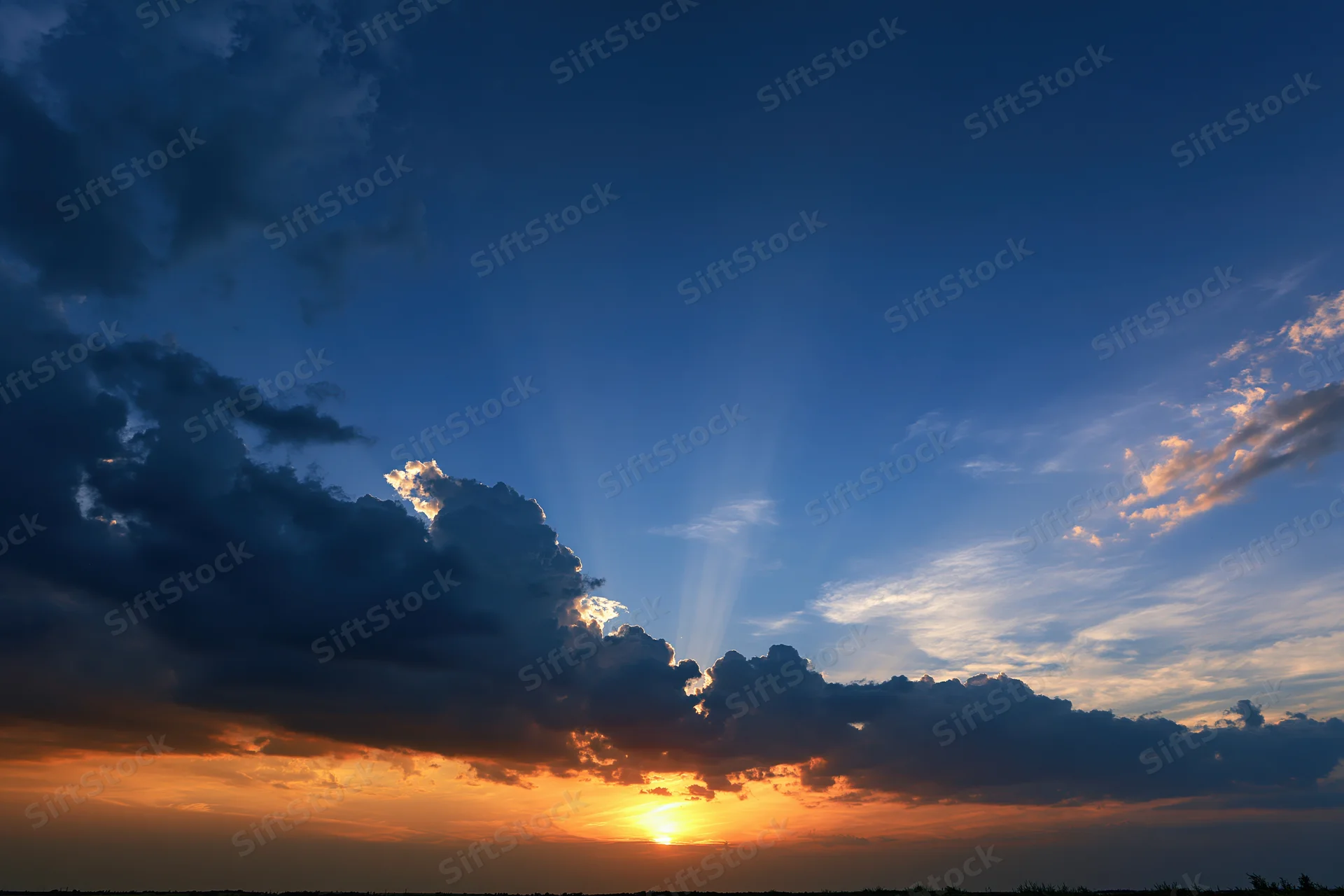 Dramatic sunset sky with crepuscular rays bursting upward from behind clouds at horizon