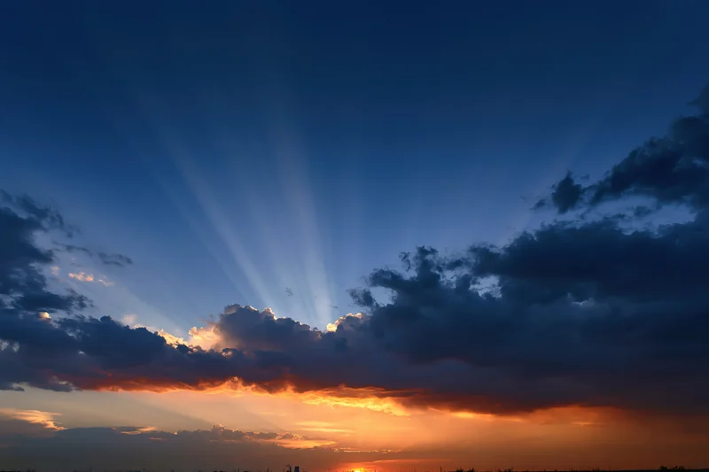 Dramatic sunset sky with crepuscular rays bursting upward from clouds at horizon