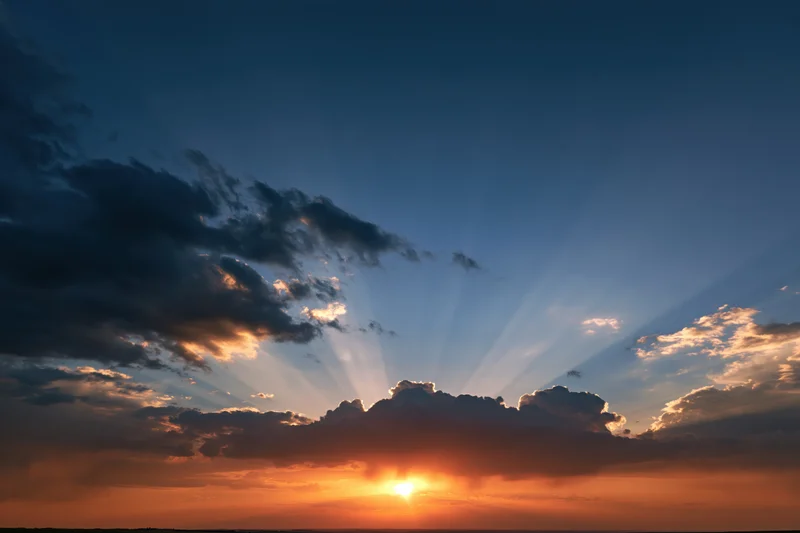 Sunset sky with crepuscular rays bursting upward from clouds at horizon