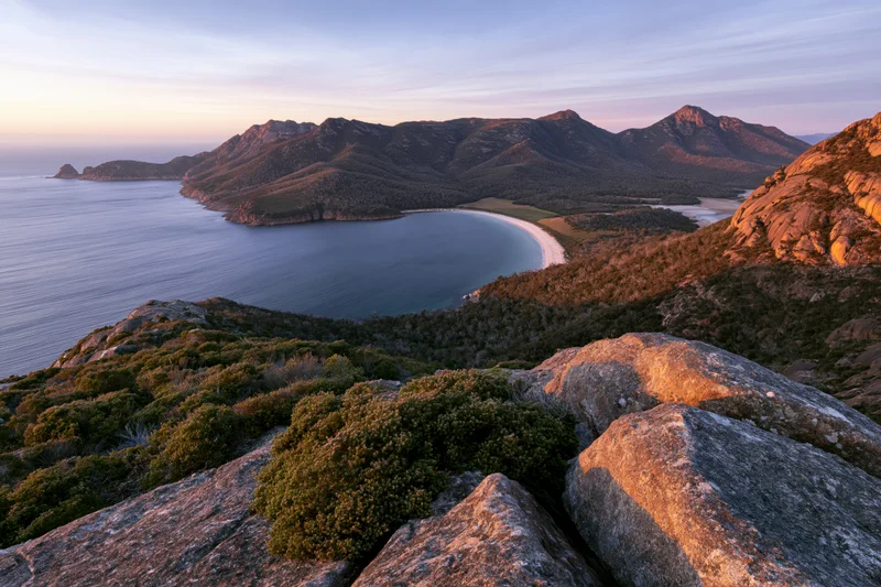 Rocky hilltop overlooking a coastal bay with mountains and ocean at sunset