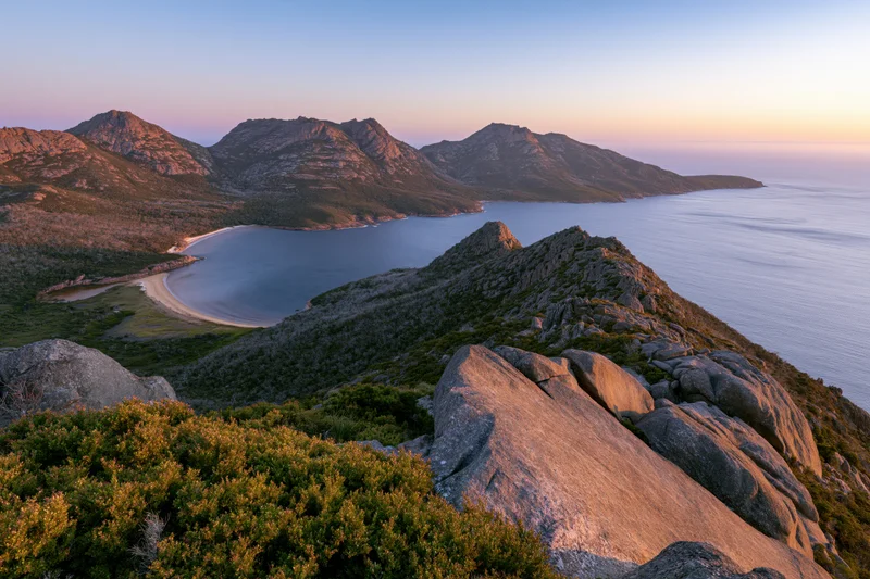 Rocky hilltop overlooking a coastal bay with mountains and ocean at sunset
