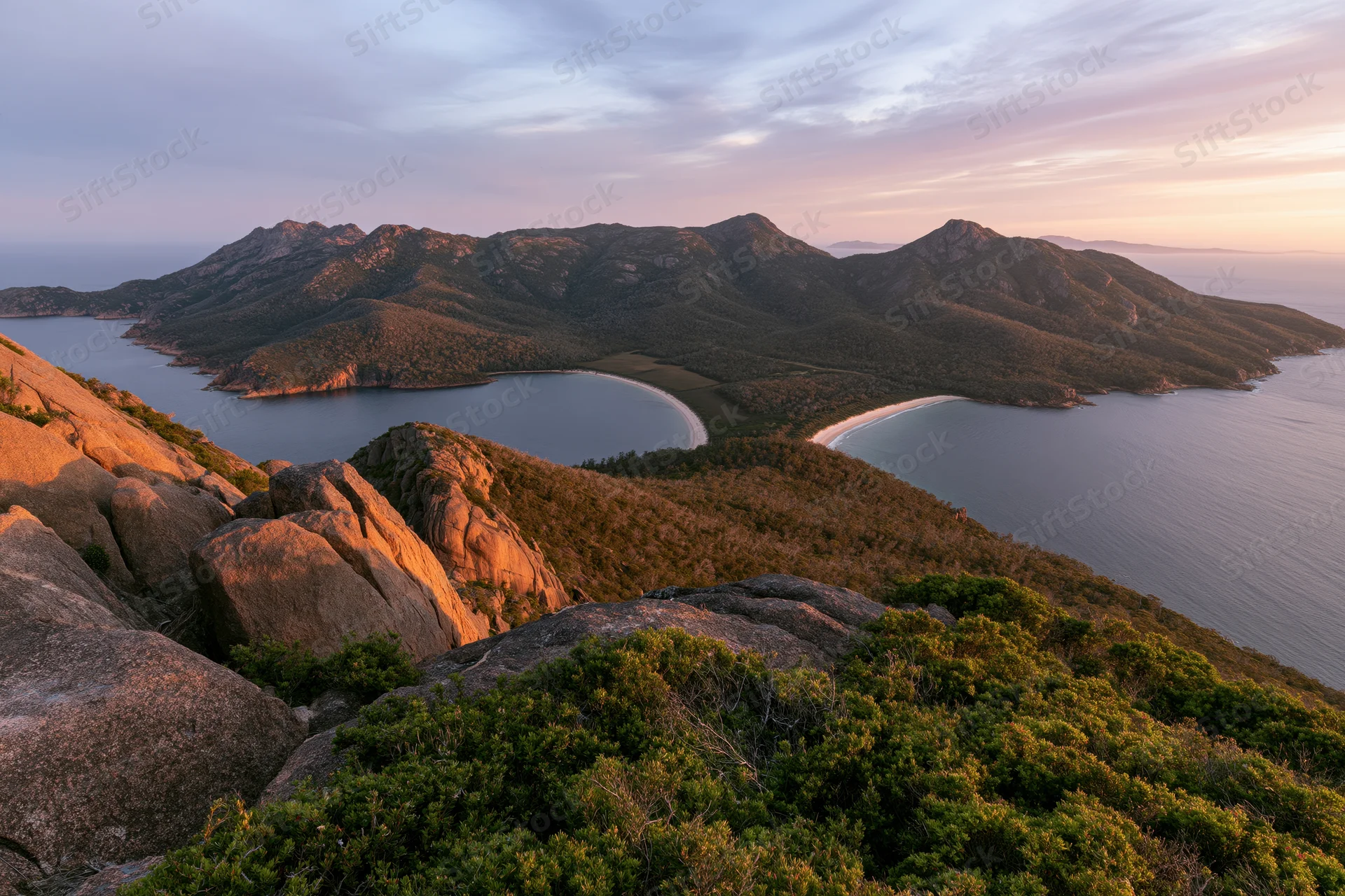 Rocky hilltop overlooking coastal mountains and bays at sunset