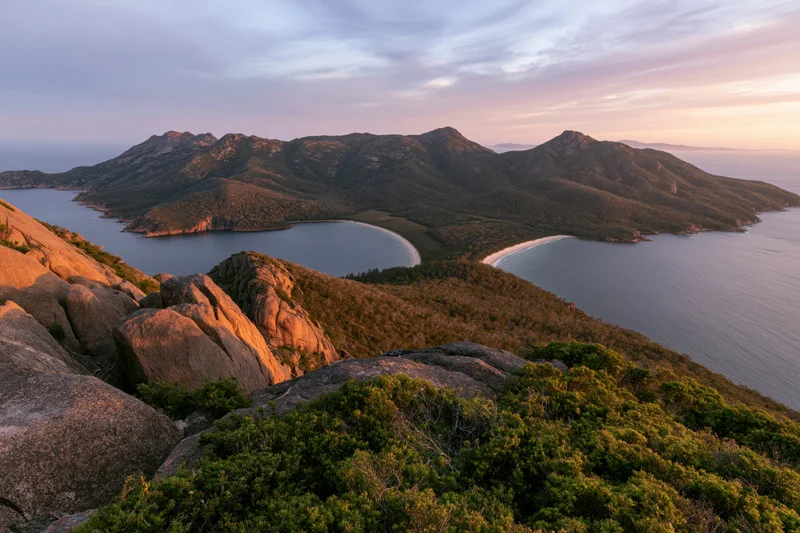 Rocky hilltop overlooking coastal mountains and bays at sunset