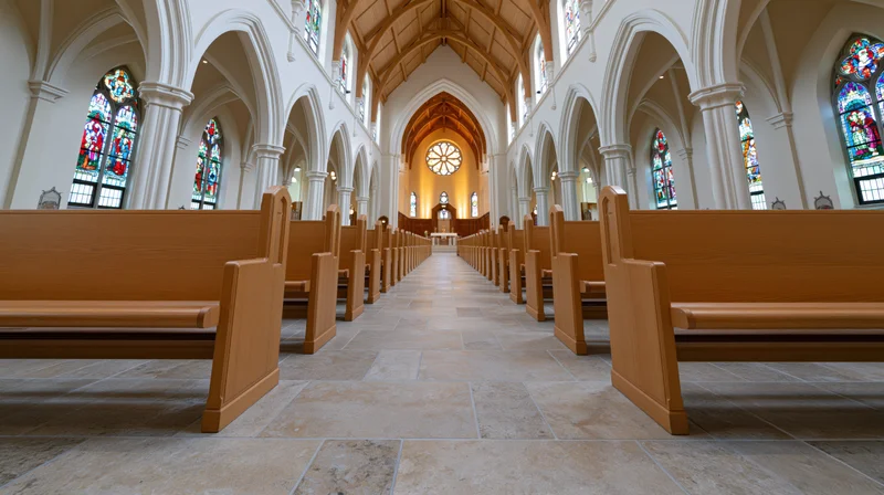Empty catholic church nave with wooden pews and stained glass windows viewed from ground level along the central aisle toward the altar
