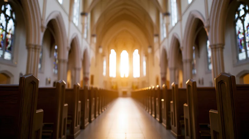 Empty catholic church nave viewed down central aisle with sunlight streaming through stained glass windows