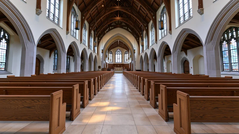 Empty church interior with wooden pews lining a central aisle toward the altar under a vaulted ceiling with arched stained glass windows