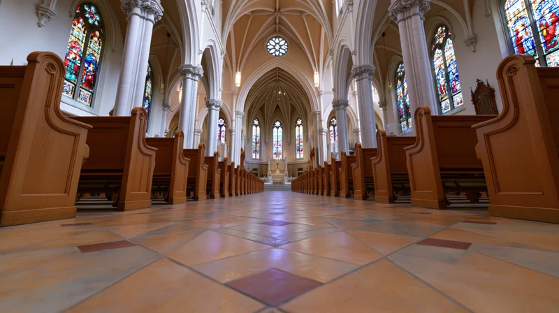 Empty church interior with rows of wooden pews leading to altar under vaulted ceiling and stained glass windows