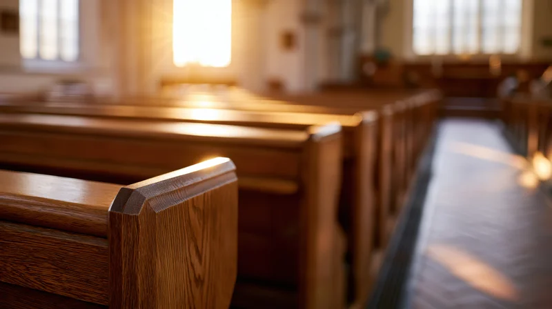 Rows of wooden pews receding into the distance inside an empty church interior with sunlight streaming through windows