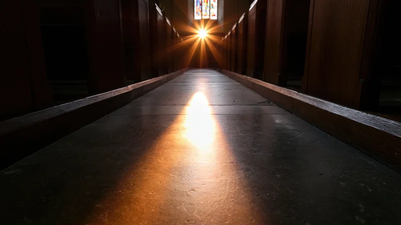 Sunlight streaming through stained glass window down empty church aisle lined with wooden pews