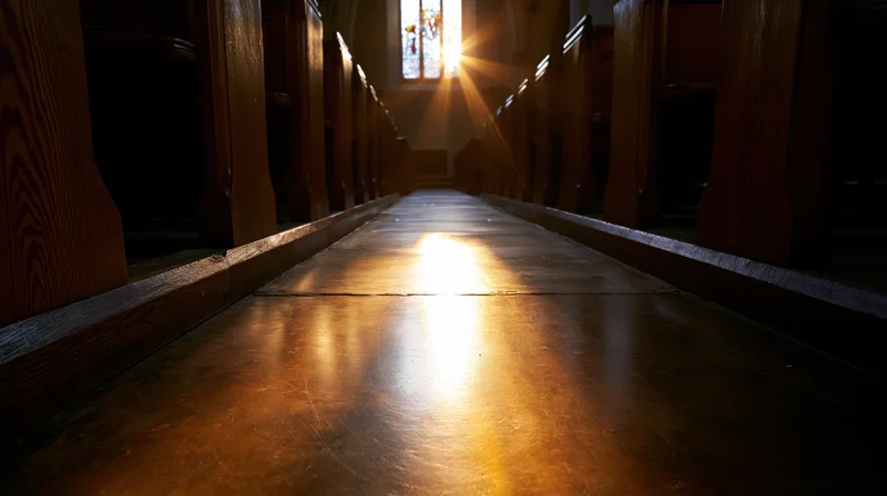 Empty church interior with wooden pews lining both sides of a central aisle illuminated by sunlight through a stained glass window