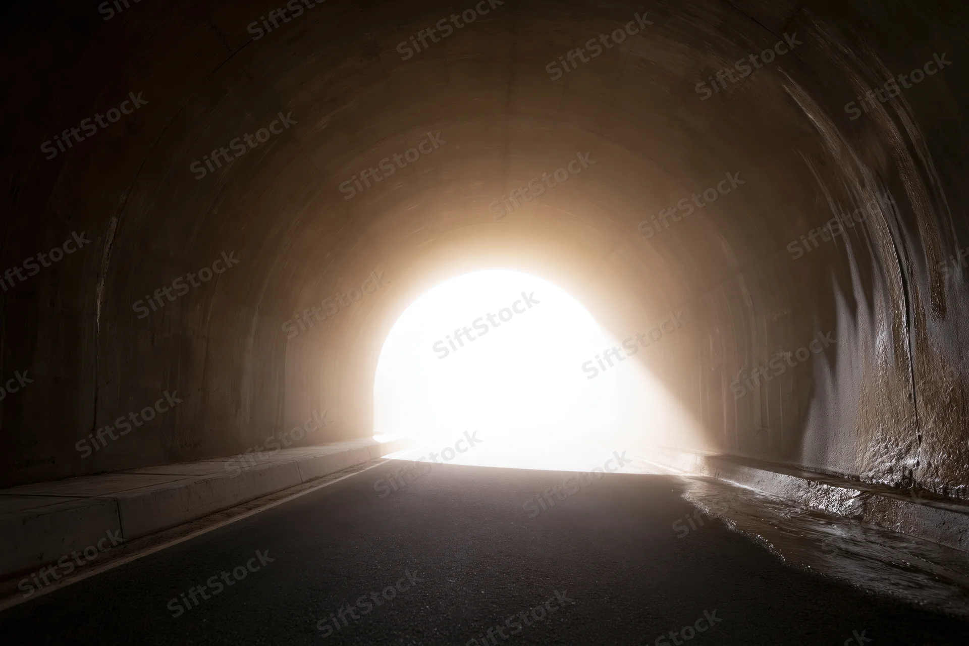 Empty concrete road tunnel viewed from inside looking toward bright exit light