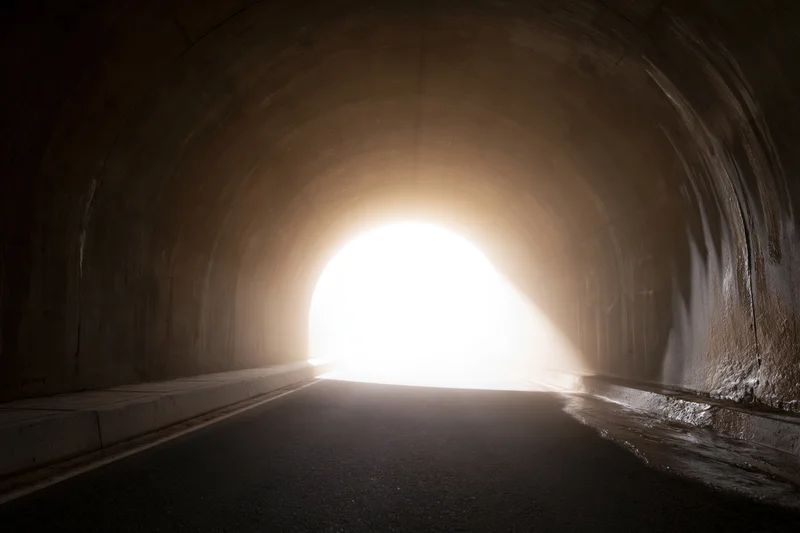 Empty concrete road tunnel viewed from inside looking toward bright exit light