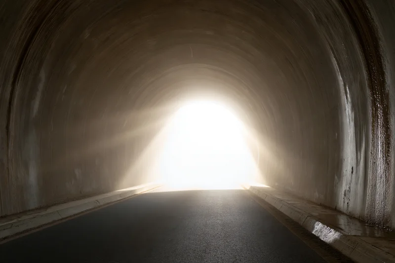 Empty concrete road tunnel viewed from inside looking toward bright exit light