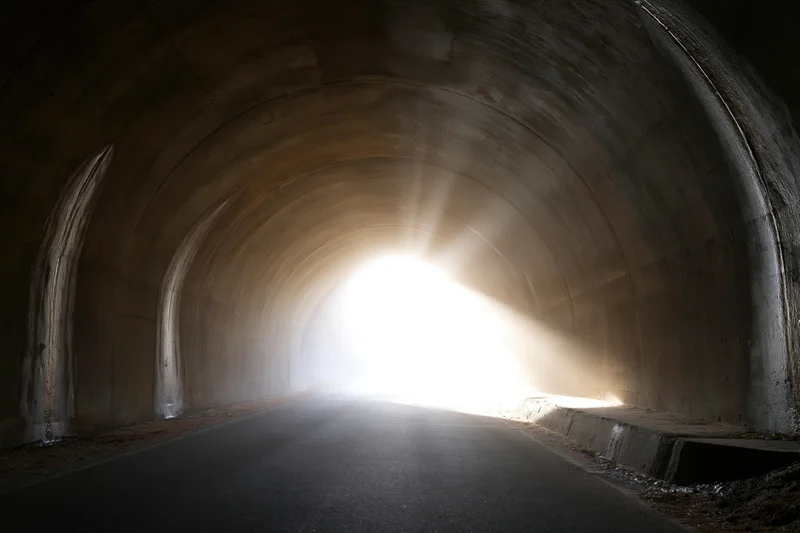 Concrete road tunnel interior viewed toward bright exit light