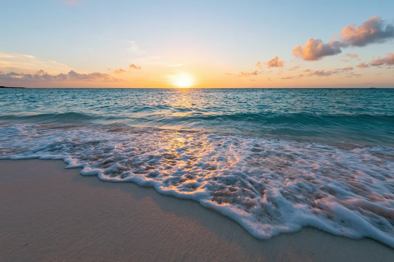 Gentle shallow wave washing onto sandy beach at sunset