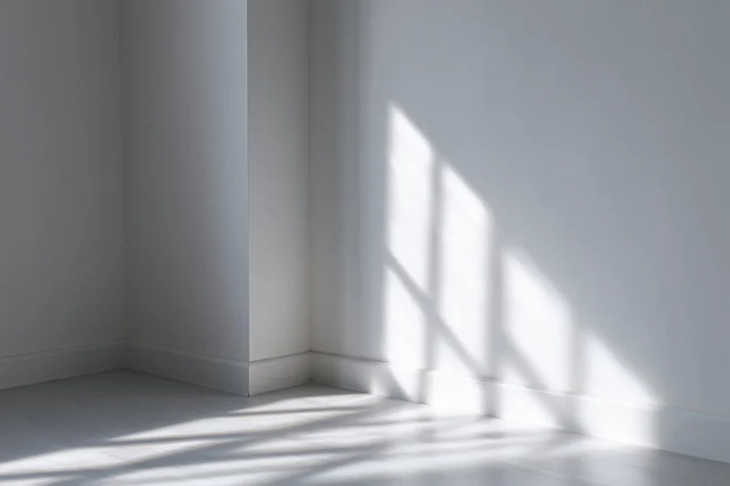Empty white room with sunlight casting window shadows on bare walls and smooth floor