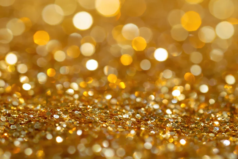 Gold glitter scattered across a surface with bokeh lights in the background