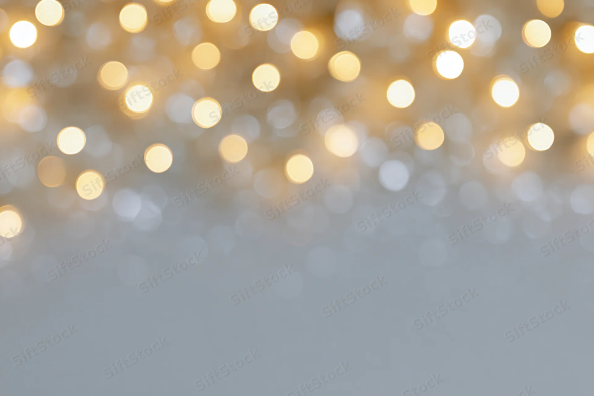 Warm white and golden bokeh lights blurred in the upper frame against a soft gray background with copyspace below