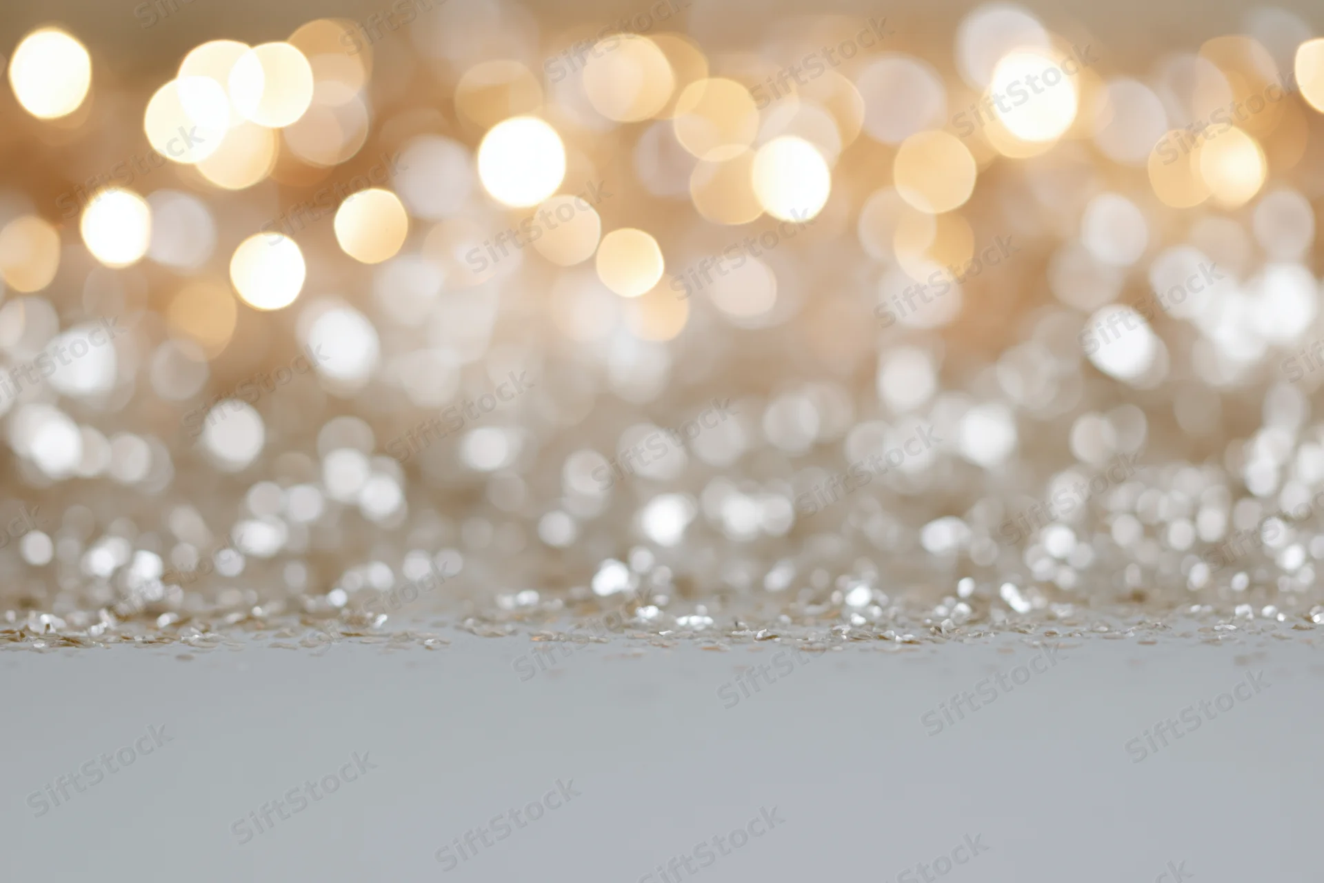 Out-of-focus warm white and gold bokeh lights with glittery surface in foreground, creating festive abstract background with copyspace