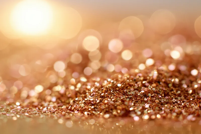 Scattered gold and bronze glitter on a warm surface with bokeh lights in the background