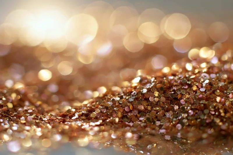 Scattered gold and bronze glitter in macro closeup with bokeh background
