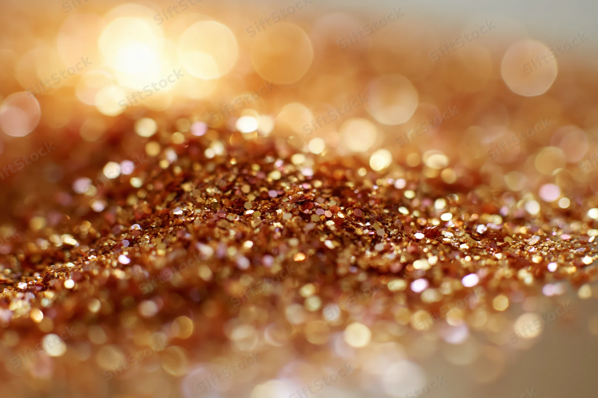 Scattered gold and bronze glitter particles on a textured surface with bokeh lights in the background