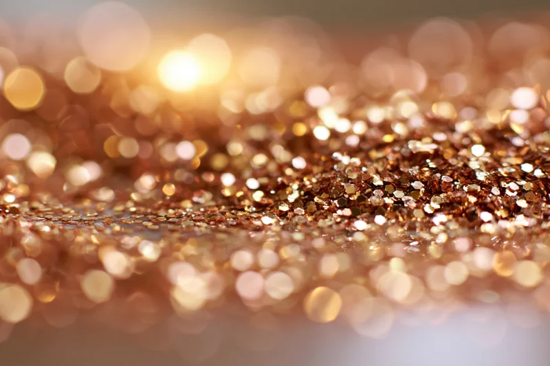 Scattered gold and bronze glitter on a textured surface with bokeh lights in the background