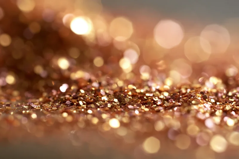 Scattered gold and bronze glitter particles on a textured surface with bokeh lights in the background