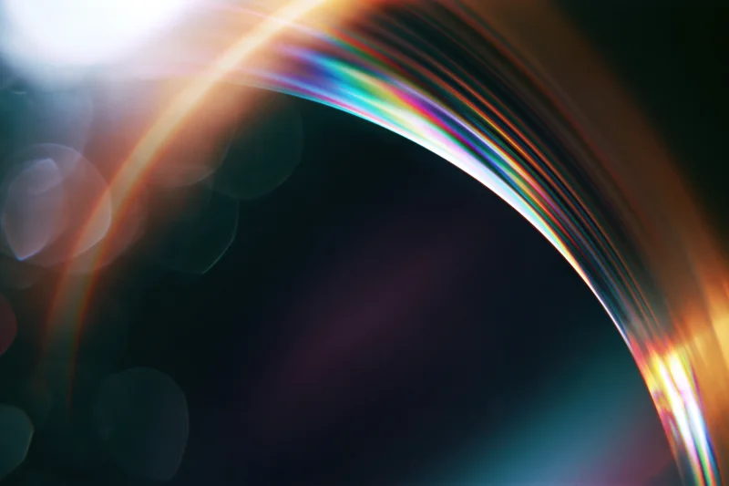 Curved glass lens reflecting rainbow light spectrum with bokeh highlights in dark background