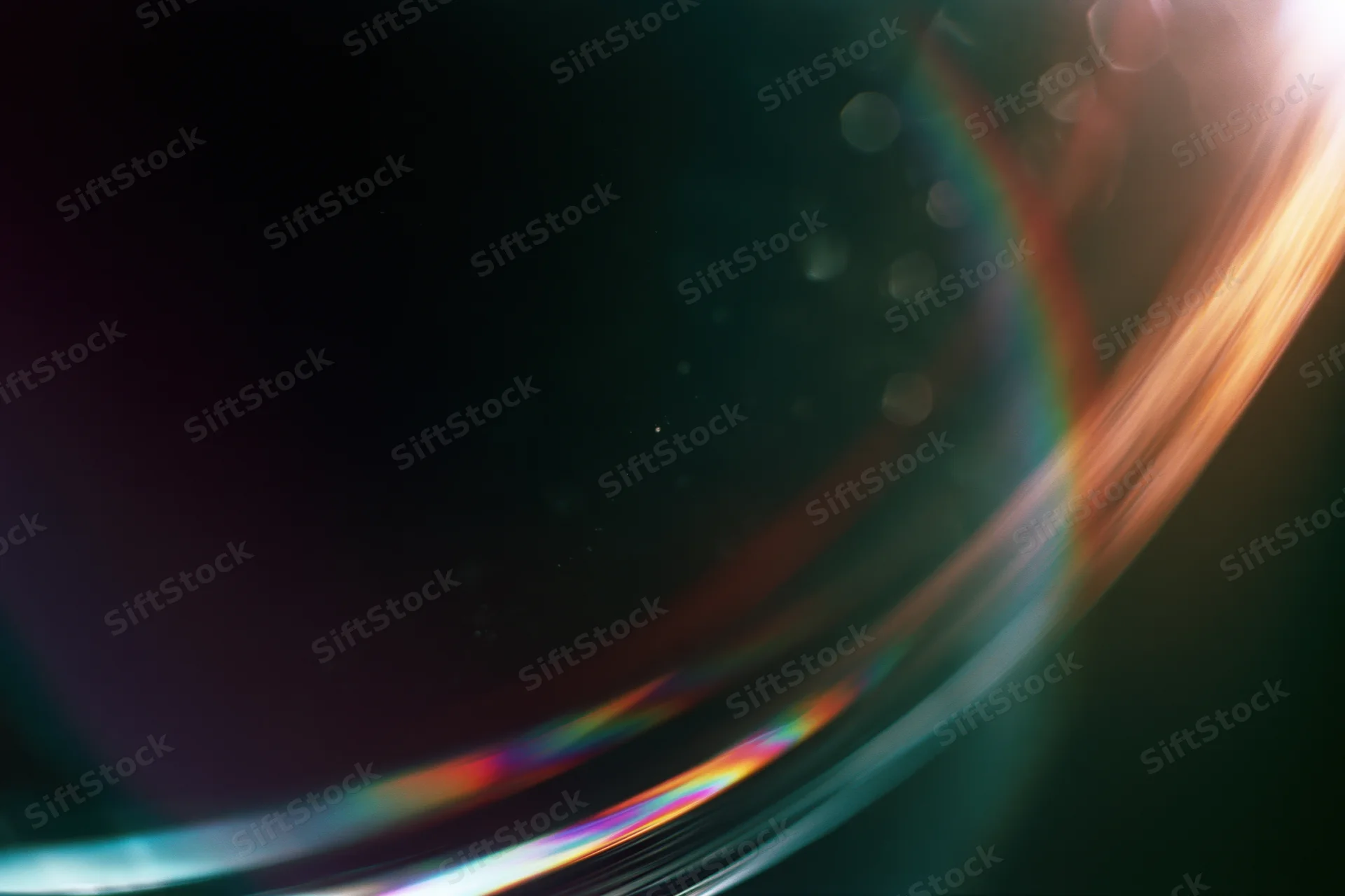 Closeup of a glass sphere reflecting rainbow light with bokeh highlights on dark background