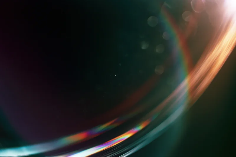 Closeup of a glass sphere reflecting rainbow light with bokeh highlights on dark background