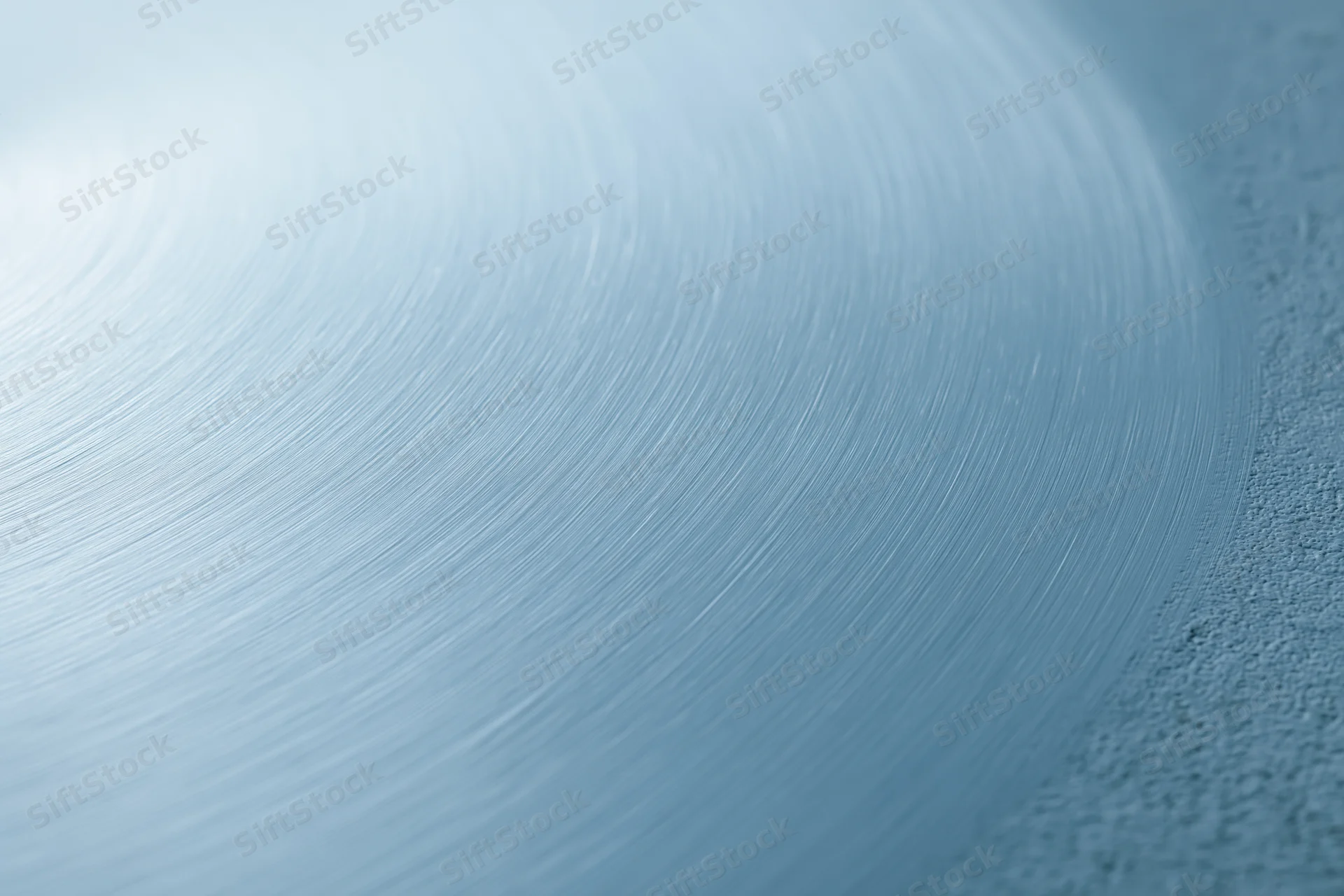 Brushed light blue metal surface filling the frame with circular texture and shallow depth of field