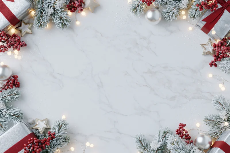 Christmas border frame with pine, berries, gifts and lights on white marble surface