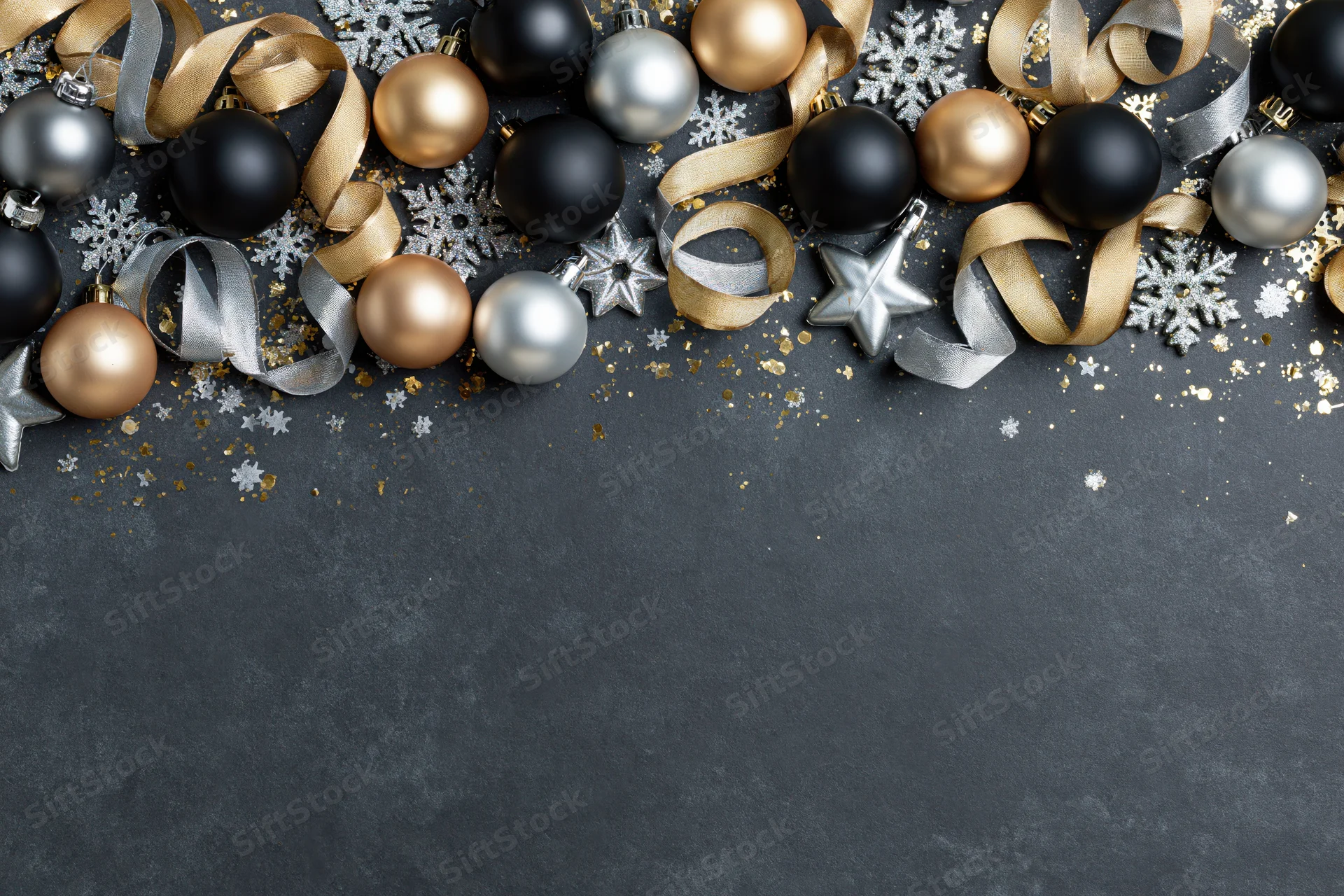 Christmas ornaments arranged along the top edge of a dark textured surface with copyspace below