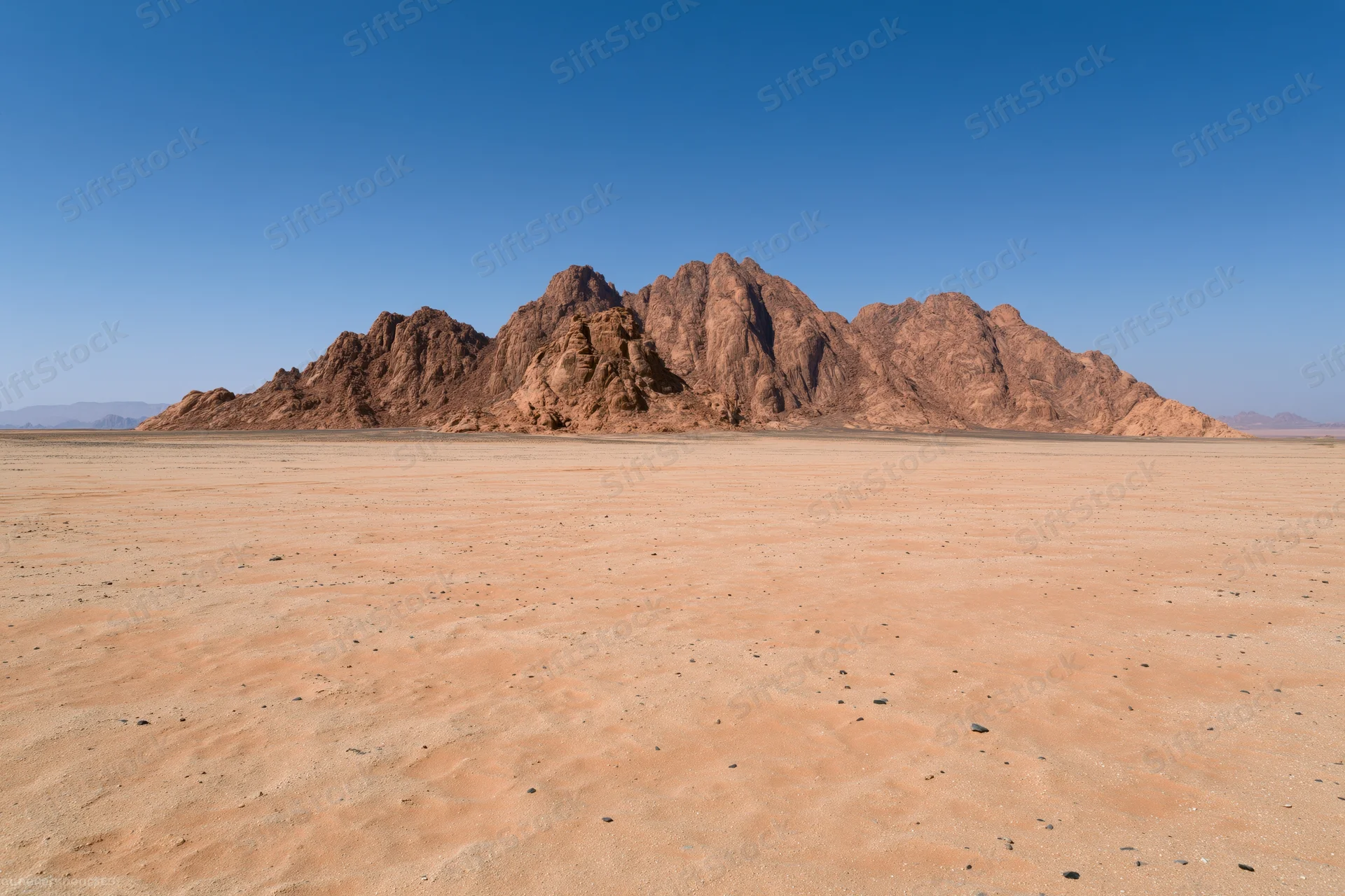 Flat desert floor stretching toward rugged sandstone mountains under clear blue sky