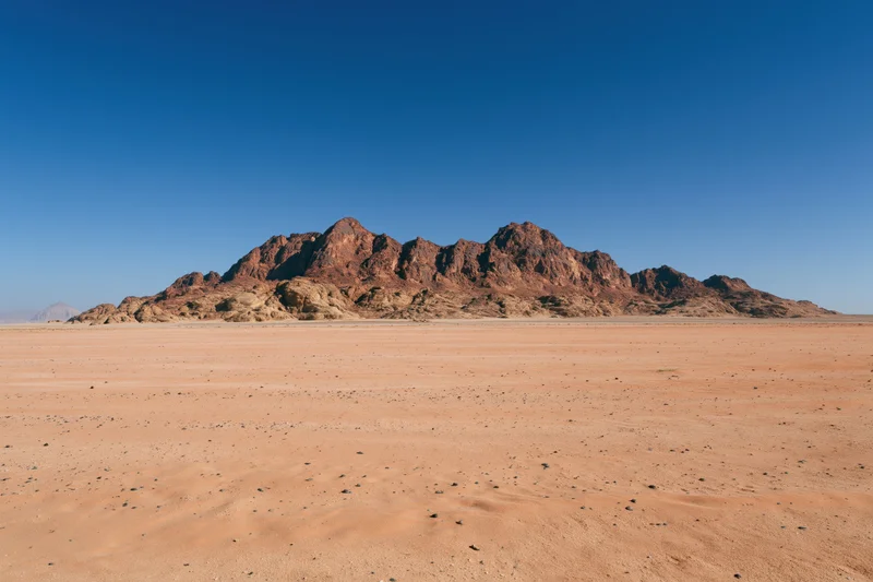 Flat desert floor stretching toward rugged sandstone mountains under clear blue sky