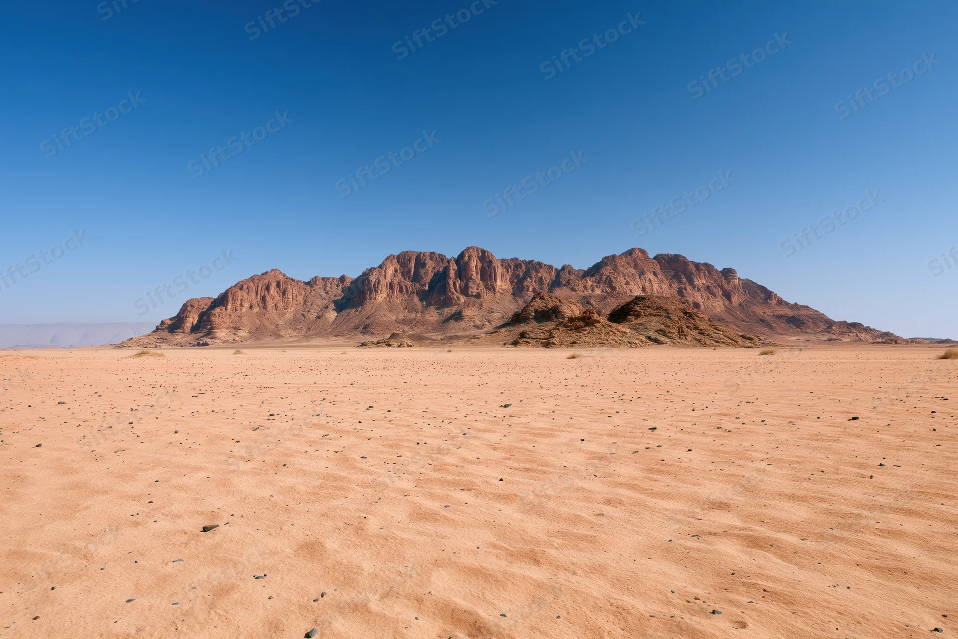 Flat desert floor stretching toward rugged sandstone mountains under clear blue sky