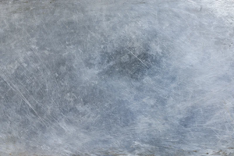 Worn metal surface covered in fine scratches and scuffs showing signs of use and abrasion