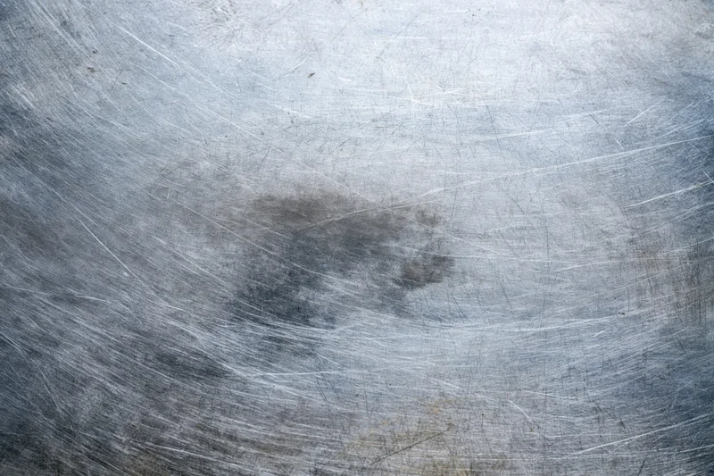 Worn metal surface with fine scratches and scuff marks showing signs of use and aging