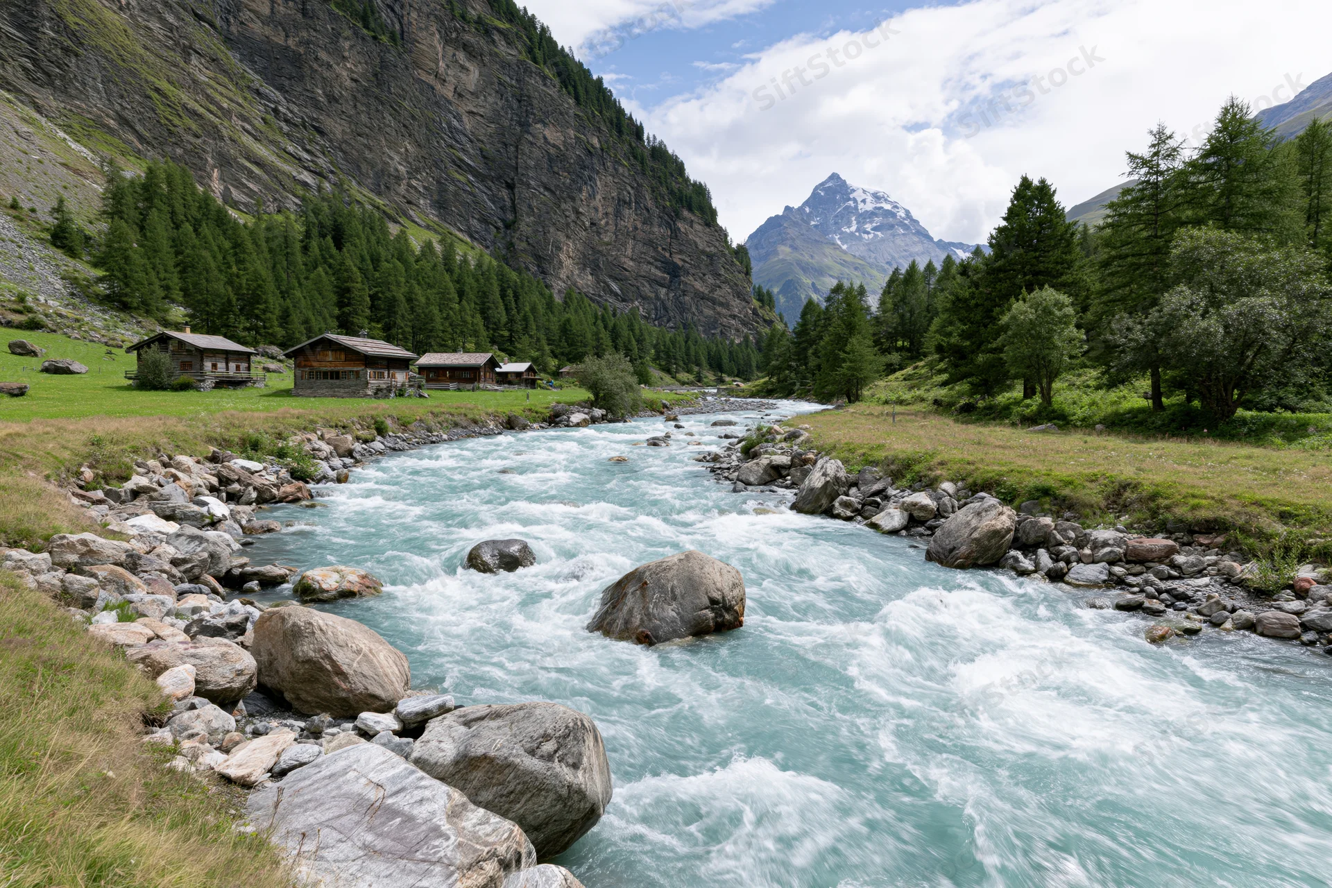 Glacial turquoise river rushing over rounded boulders through alpine valley with wooden cabins and pine forest