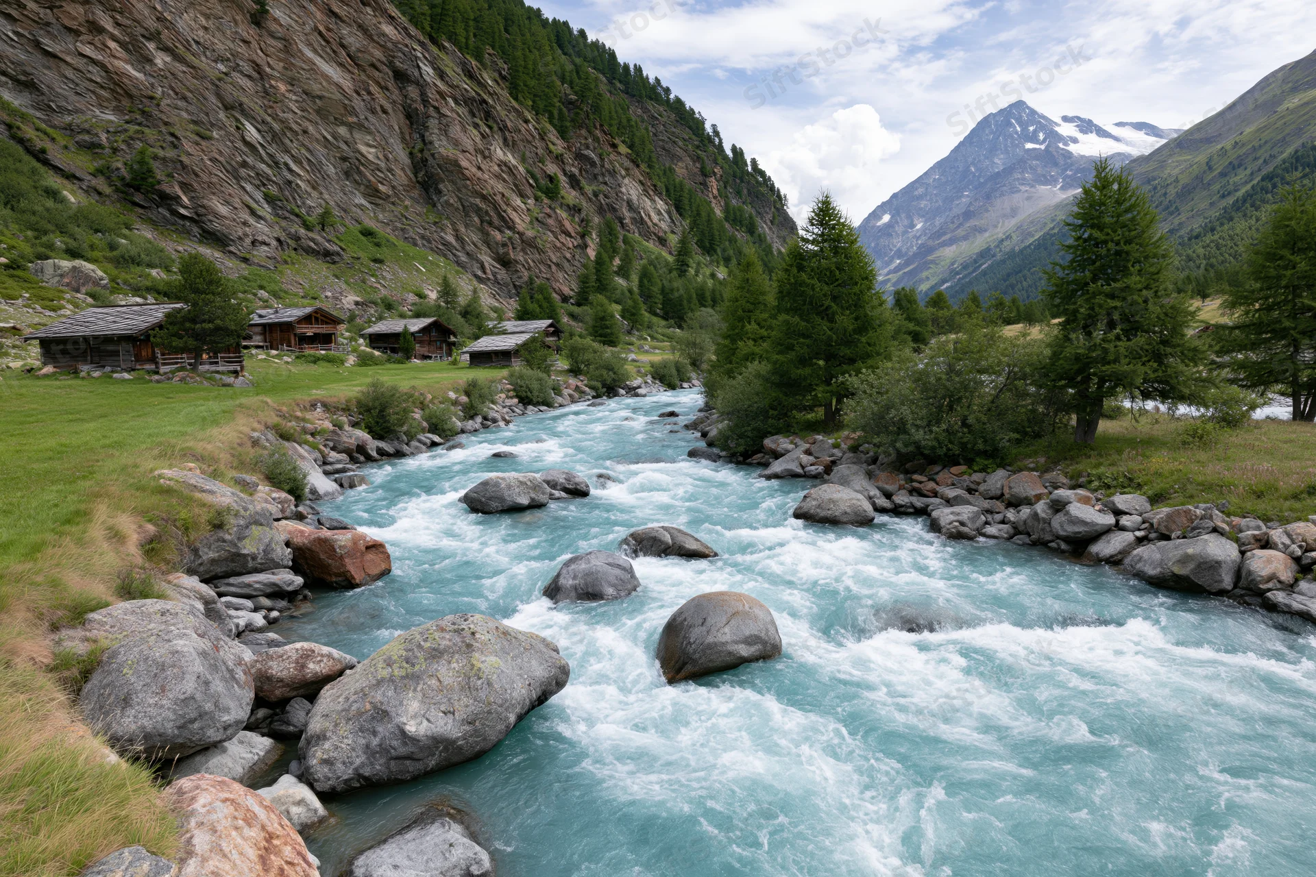 Glacial turquoise river rushing over rounded boulders through alpine valley with wooden cabins and pine trees