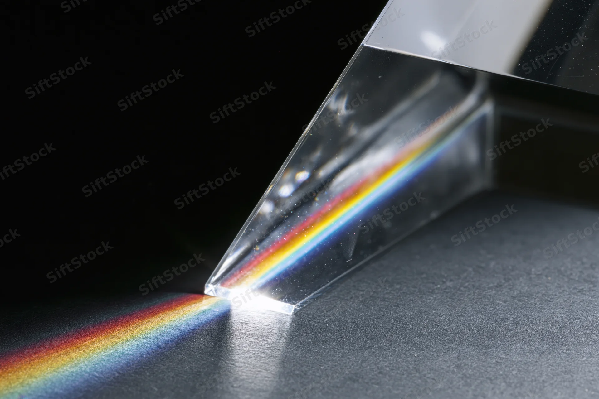 Glass prism dispersing white light into a rainbow spectrum on a dark surface