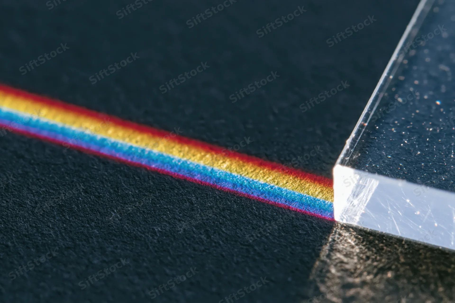Glass prism refracting a narrow beam of white light into a visible spectrum on a dark surface