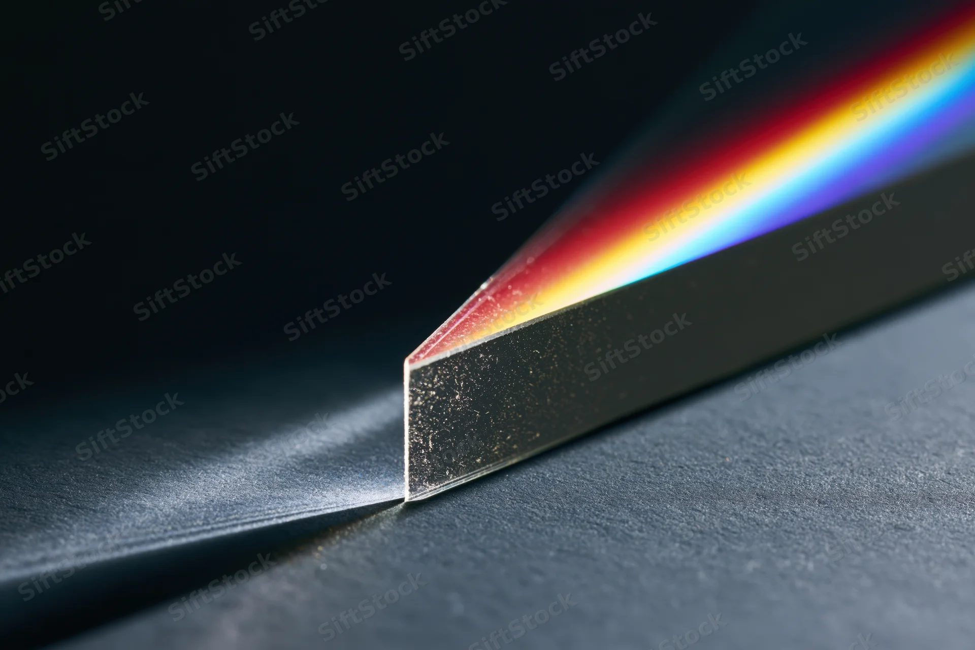 Glass prism refracting white light into a rainbow spectrum on a dark surface