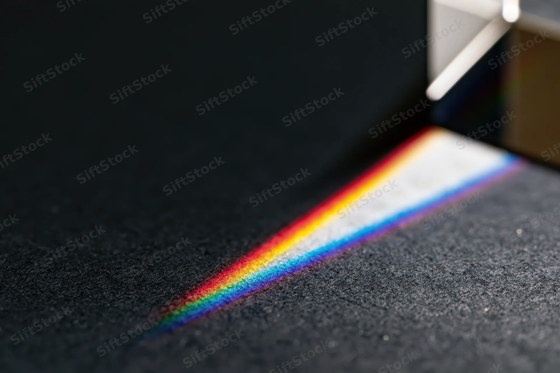 Glass prism refracting a white light beam into a rainbow spectrum on a dark carpeted floor